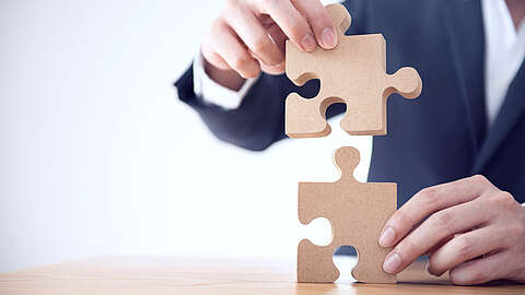 Zwei Puzzleteile werden von einer Person im Anzug zusammengesetzt