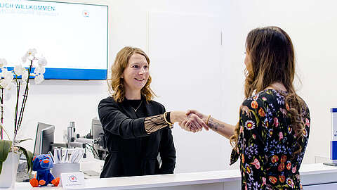 Zwei Frauen schütteln sich am Empfang zur Begrüßung die Hand