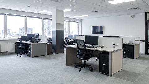 Arbeitsplatz mit moderner IT-Hardware Ein modernes Großraumbüro mit mehreren leeren Schreibtischen, Bürostühlen, Computern und großen Fenstern, die natürliches Licht hereinlassen. Der Raum ist sauber und hell, die Möbel sind in neutralen Farben gehalten und der Boden ist mit Teppich ausgelegt.